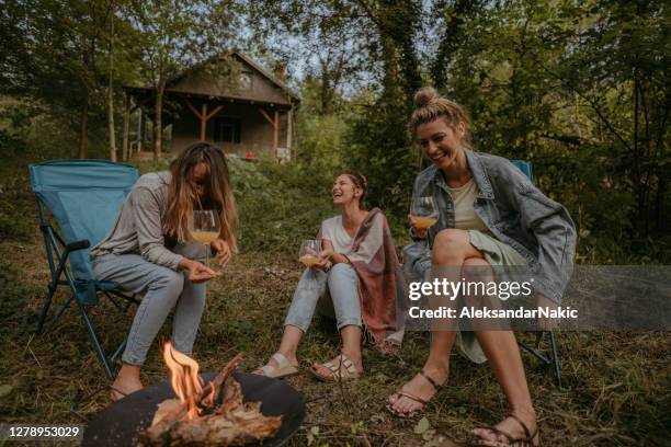 jonge vrouwen die door kampvuur zitten - haardvuur stockfoto's en -beelden