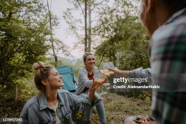 young women sitting by campfire and sipping wine - open fire stock pictures, royalty-free photos & images