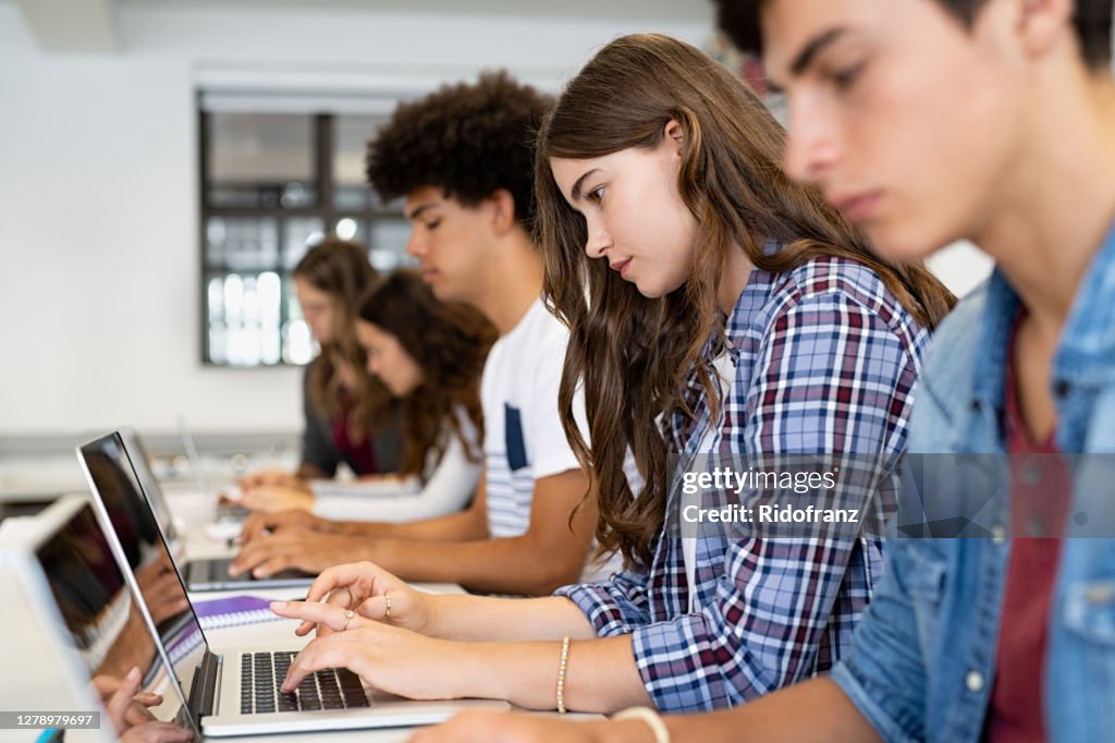 Group of high school students using laptop in classroom