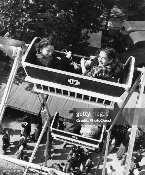 View of a pair of girls who look back at the camera during a Ferris wheel ride at a county fair, Lancaster, Ohio, 1949.
