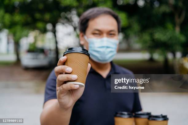 asian deliveryman wearing face mask sending take out coffee to customer - takeaway coffee cup stock pictures, royalty-free photos & images