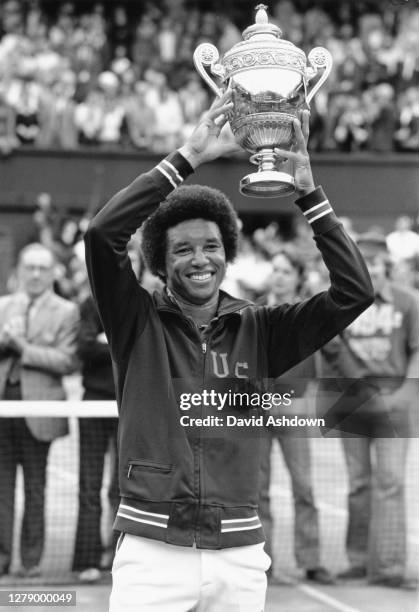 Arthur Ashe of the United States wearing his USA emblazoned Davis Cup warm-up jacket holds aloft the Gentleman's Singles Trophy on Centre Court after...