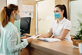 Health spa receptionist and her customer wearing face masks due to coronavirus pandemic.