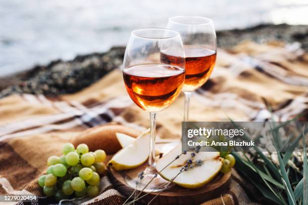 two glasses of wine and summer fruits on the beach, sea and landscape in background, summer picnic, idea for outdoor weekend activity - roses stockfoto's en -beelden