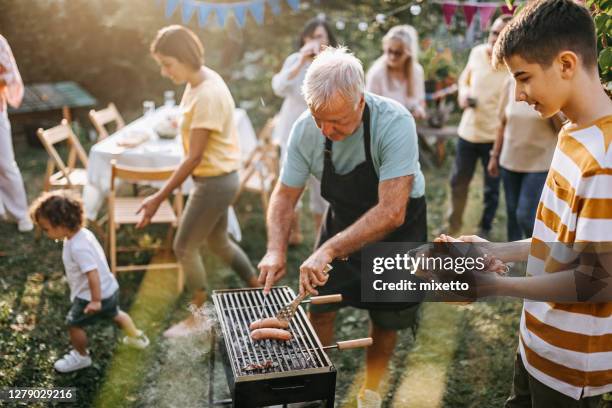 großvater serviert wurst zu teenager-enkel - familie grillen stock-fotos und bilder