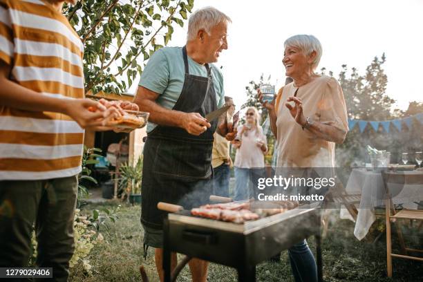 happy senior coupe with man cooking hot dogs on barbecue for family - couple grilling stock pictures, royalty-free photos & images