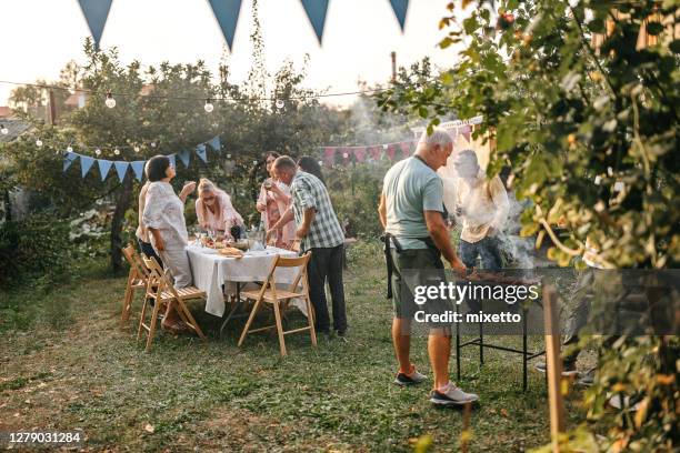 senior mann macht grillen für seine freunde während gartenparty - gartenparty stock-fotos und bilder