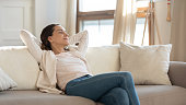 Confident millennial female enjoying tranquility relaxing on sofa indoors