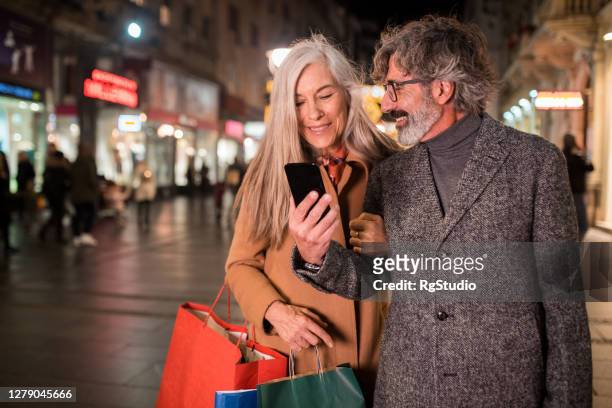 mature couple using smartphone during their christmas shopping - holiday shopping stock pictures, royalty-free photos & images