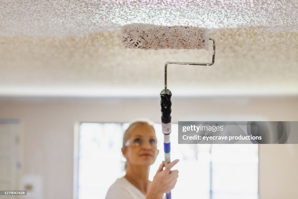 Mature Adult Female Painting Ceiling White With Paint Roller