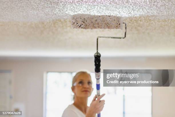 mature adult female painting ceiling white with paint roller - textured ceiling stock pictures, royalty-free photos & images