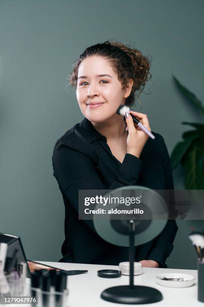 jeune femme latine appliquant le maquillage et souriant à l’appareil-photo - applying stock photos et images de collection