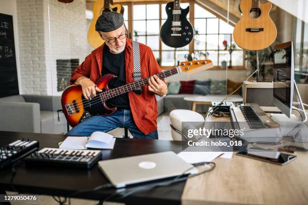porträt eines älteren musikers mit e-gitarre in seinem musikstudio sitzend - bassgitarre stock-fotos und bilder