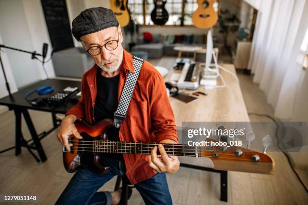 porträt eines älteren musikers mit e-gitarre in seinem musikstudio sitzend - bassgitarre stock-fotos und bilder