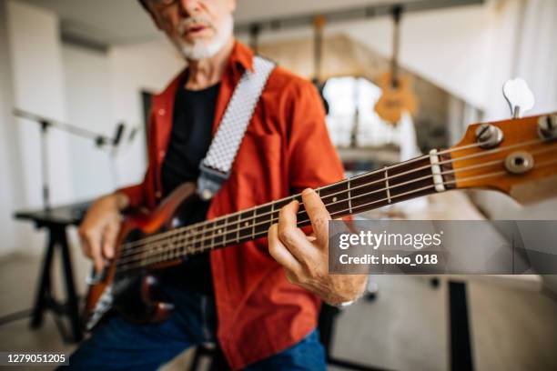 porträt eines älteren musikers mit e-gitarre in seinem musikstudio sitzend - bassgitarre stock-fotos und bilder