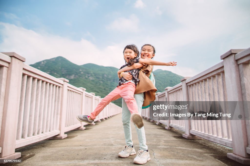 Little sibling playing joyfully on bridge in sunny day