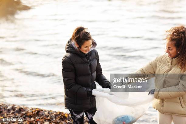Smiling female environmentalists collecting microplastics against lake