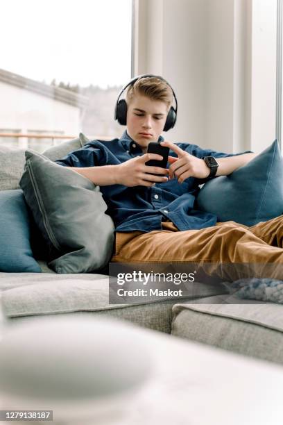 teenage boy using smart phone while wearing headphones at home - boy headphones stock-fotos und bilder