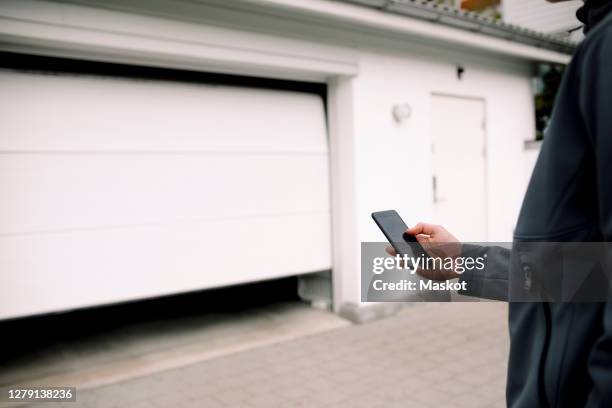 midsection of teenage boy entering pin in smart phone while unlocking garage - safety pin stockfoto's en -beelden