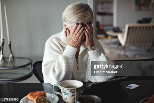 worried senior woman with head in hands sitting by dining table at home - head in hands stock pictures, royalty-free photos & images