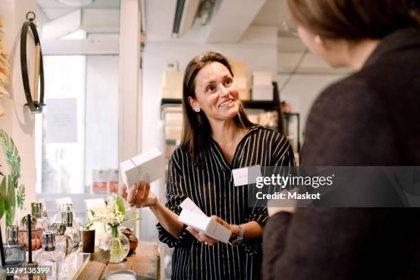 smiling saleswoman with perfume box talking to customer at store - perfumería fotografías e imágenes de stock
