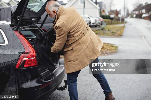 senior man keeping golf bag in car trunk during winter - auto von hinten winter stock-fotos und bilder