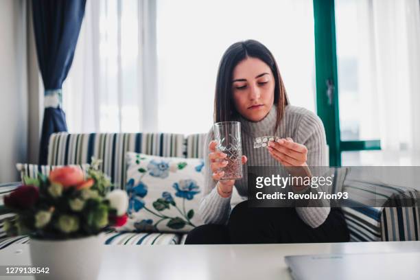 close up of sick young woman holding a glass of water and medication in her hand - diabetes pills stock pictures, royalty-free photos & images
