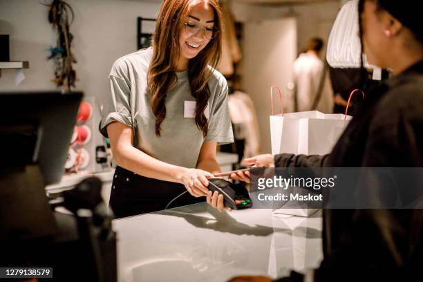 female customer paying through smart phone to smiling saleswoman at store - payer photos et images de collection