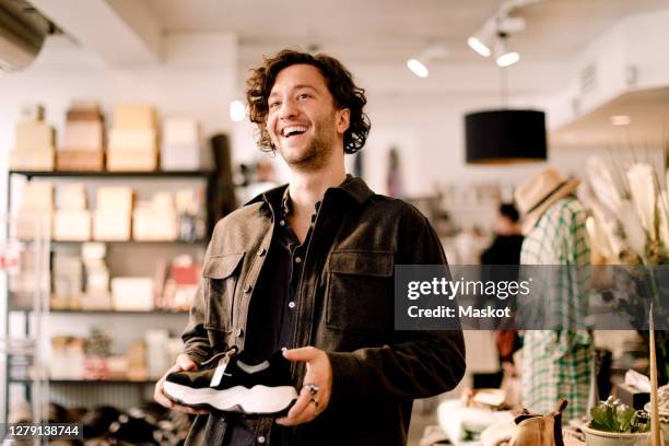 happy male customer looking away while buying shoe at retail store - detailhandel stockfoto's en -beelden