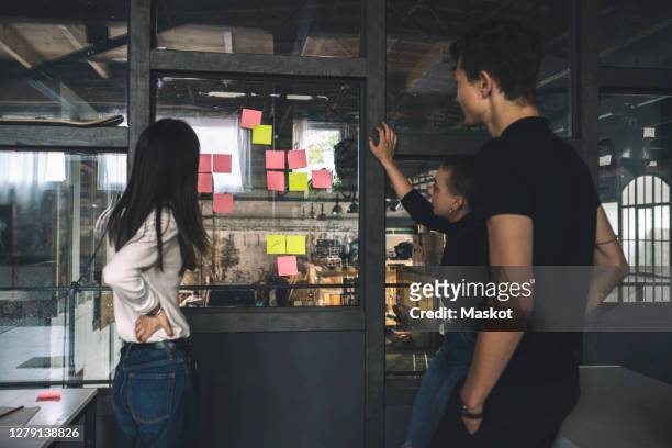 male an female coworkers reading sticky notes on glass door at workplace - brainstorming stock-fotos und bilder
