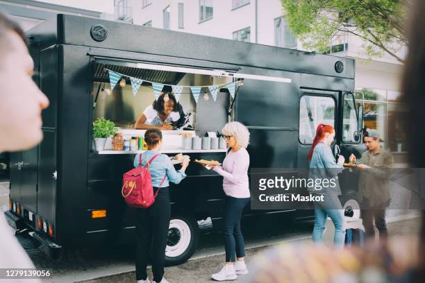 female owner giving street food to customers while standing in commercial land vehicle - foodtruck stockfoto's en -beelden