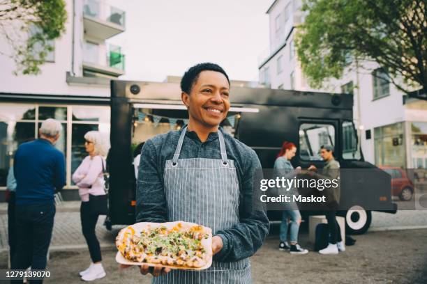 smiling male owner with indian food plate looking away in city - indian food stockfoto's en -beelden