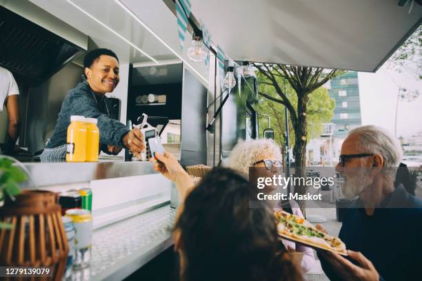 smiling owner giving credit card reader to customer for payment while standing in food truck - food truck payments stock pictures, royalty-free photos & images