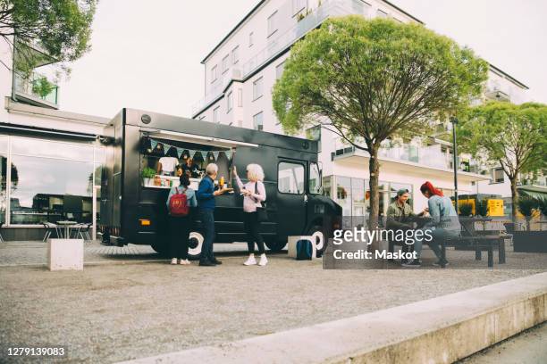 male and female customers waiting near commercial land vehicle for indian food in city - foodtruck stockfoto's en -beelden
