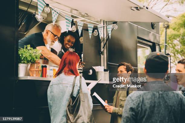 owner with assistant talking to smiling customers by food truck - foodtruck stockfoto's en -beelden