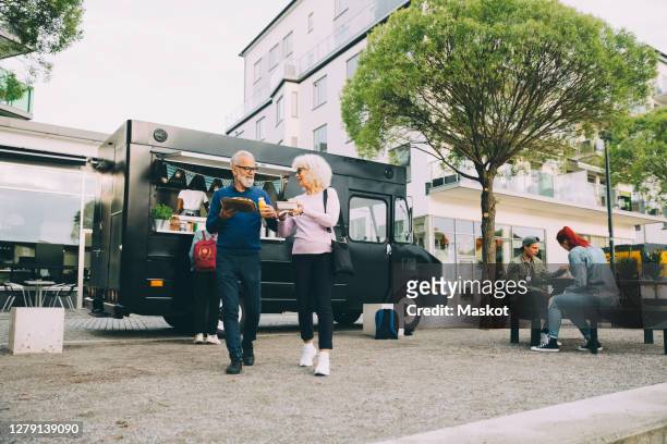senior male and female customers with street food walking against commercial land vehicle in city - food truck street stock pictures, royalty-free photos & images