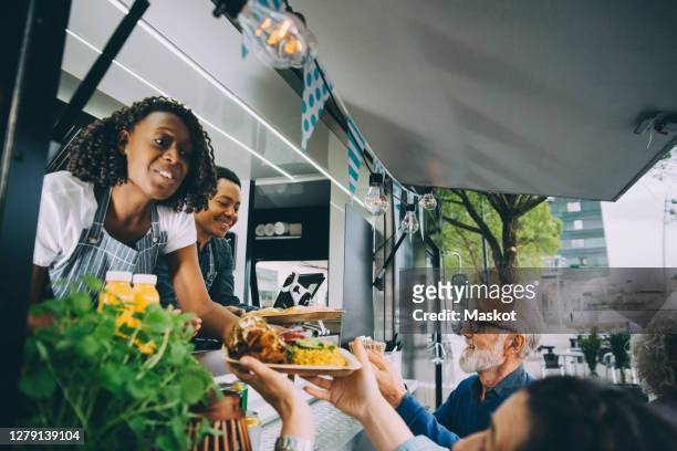 smiling owners giving indian food to customers while standing in commercial land vehicle - foodtruck stockfoto's en -beelden