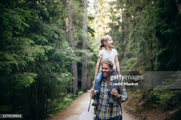 smiling father carrying daughter on shoulder while walking in forest - ballade famille photos et images de collection