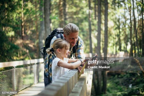 smiling father with backpack and daughter looking at smart phone in forest - family nature phone stock pictures, royalty-free photos & images