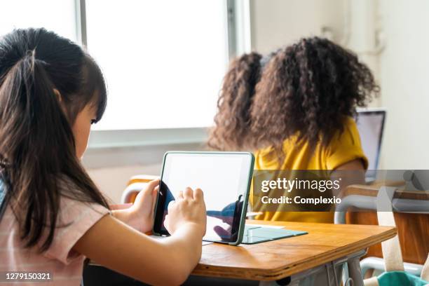 grundskoleflickor som använder digital enhet i skolans klassrum, digital infödd, teknik, inlärning, pekskärm. kvinnliga elever i klassen bakifrån - day 7 bildbanksfoton och bilder