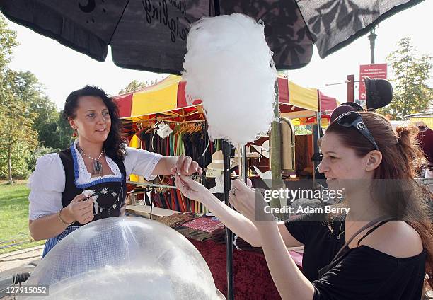 Vendor wearing a traditional Bavarian dirndl serves a customer cotton candy during an outdoor festival to celebrate German Unity Day on the 21st...