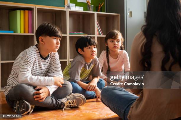 multiethnische gruppe von schulkindern, die auf dem boden sitzen und zuhören - singapore school stock-fotos und bilder