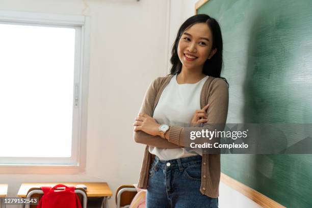 young female asian teacher smiling by blackboard in school classroom - korean female stock pictures, royalty-free photos & images