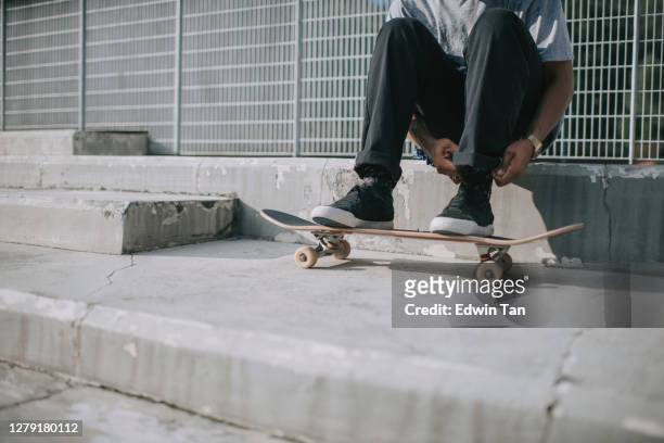 スケートボードパークでスケートボードを練習する前に靴を結ぶアジアのスケートボーダー - tied up ストックフォトと画像