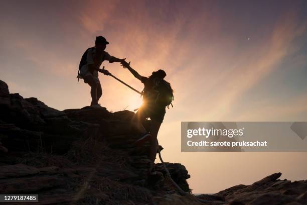 silhouette male and female hikers climbing up  mountain cliff . helps and team work concept. - berge besteigung erfolg business stock-fotos und bilder