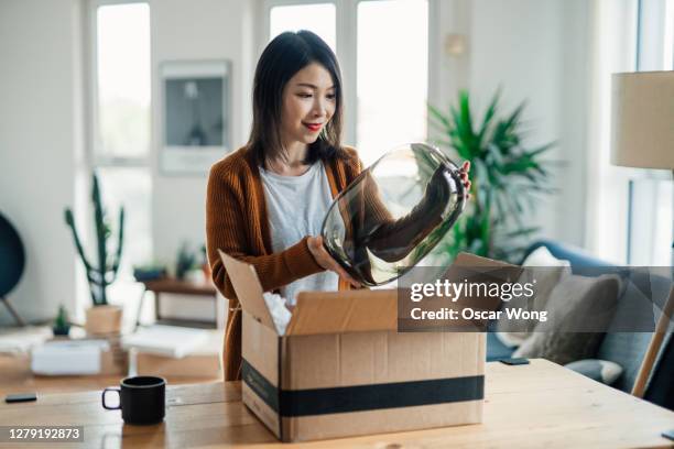 cheerful young woman opening a delivery box at home - boxes home stock-fotos und bilder