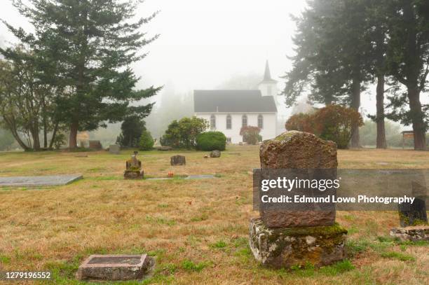 headstones in a small cemetery behind a white wooden church. - north pacific stock pictures, royalty-free photos & images