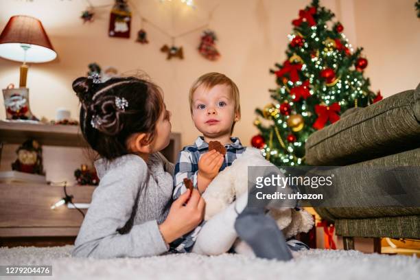 mädchen essen kekse unter weihnachtsbaum - children only stock-fotos und bilder