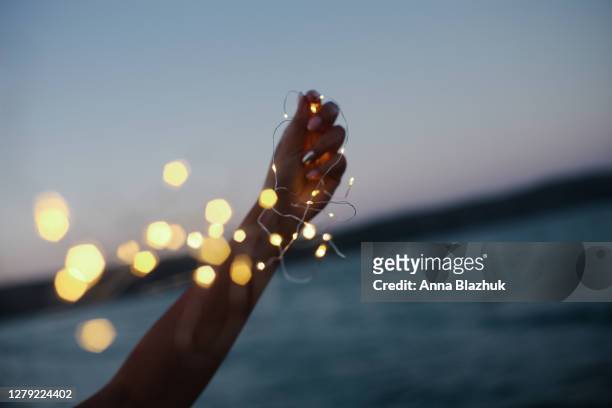 string lights close up in female hand against blue sea background. romantic picture of event, festival or holiday outdoors - summer lights stockfoto's en -beelden