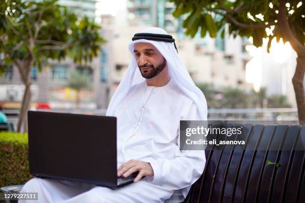 arabischer geschäftsmann arbeitet mit laptop im freien in dubai marina - emirati guy using laptop stock-fotos und bilder